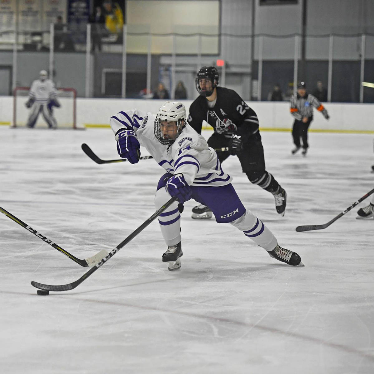 A Chatham hockey player skates with the puck during a game, with an opponent behind