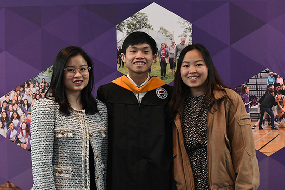 A graduating student in robes poses with two family members, all of whom are smiling broadly on Commencement Day