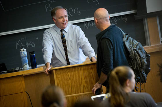 Photo of Chatham University professor leaning over a lectern, speaking with a student