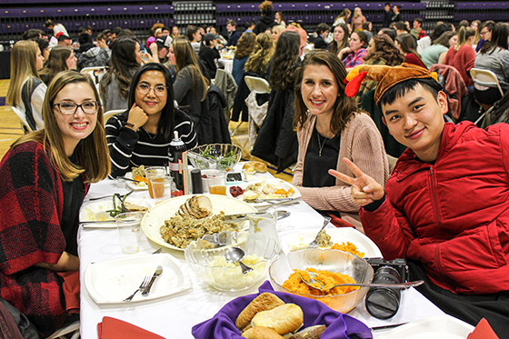 Photo of international students at a Chatham University harvest dinner, smiling for the camera as they eat dinner