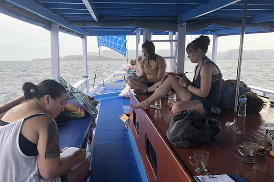 Photo of a group of MFACW students on a boat in Indonesia, writing