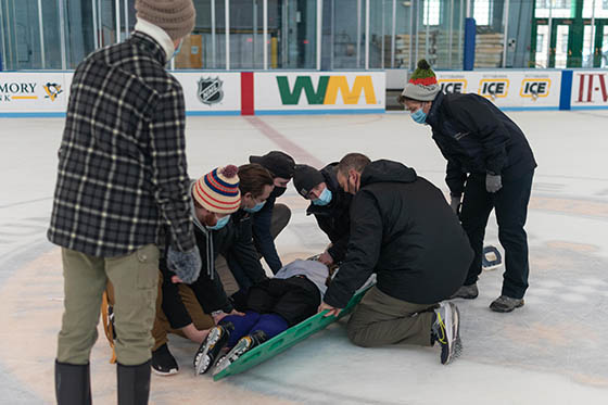 Photo of MSAT students wearing masks on an ice rink, helping an injured hockey player who is laying on the ice