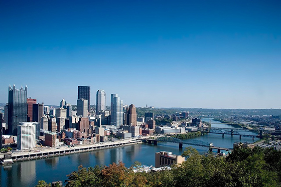 Photo of the Pittsburgh, Pennsylvania skyline featuring tall buildings, rivers, bridges, and blue skies