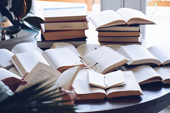 Photo of many books laying open on a circular table with a pair of glasses in the middle. 