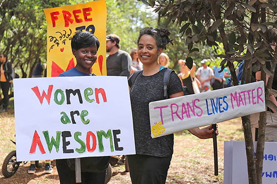 Photo of two women holding protest signs reading Trans Lives Matter and Women Are Awesome