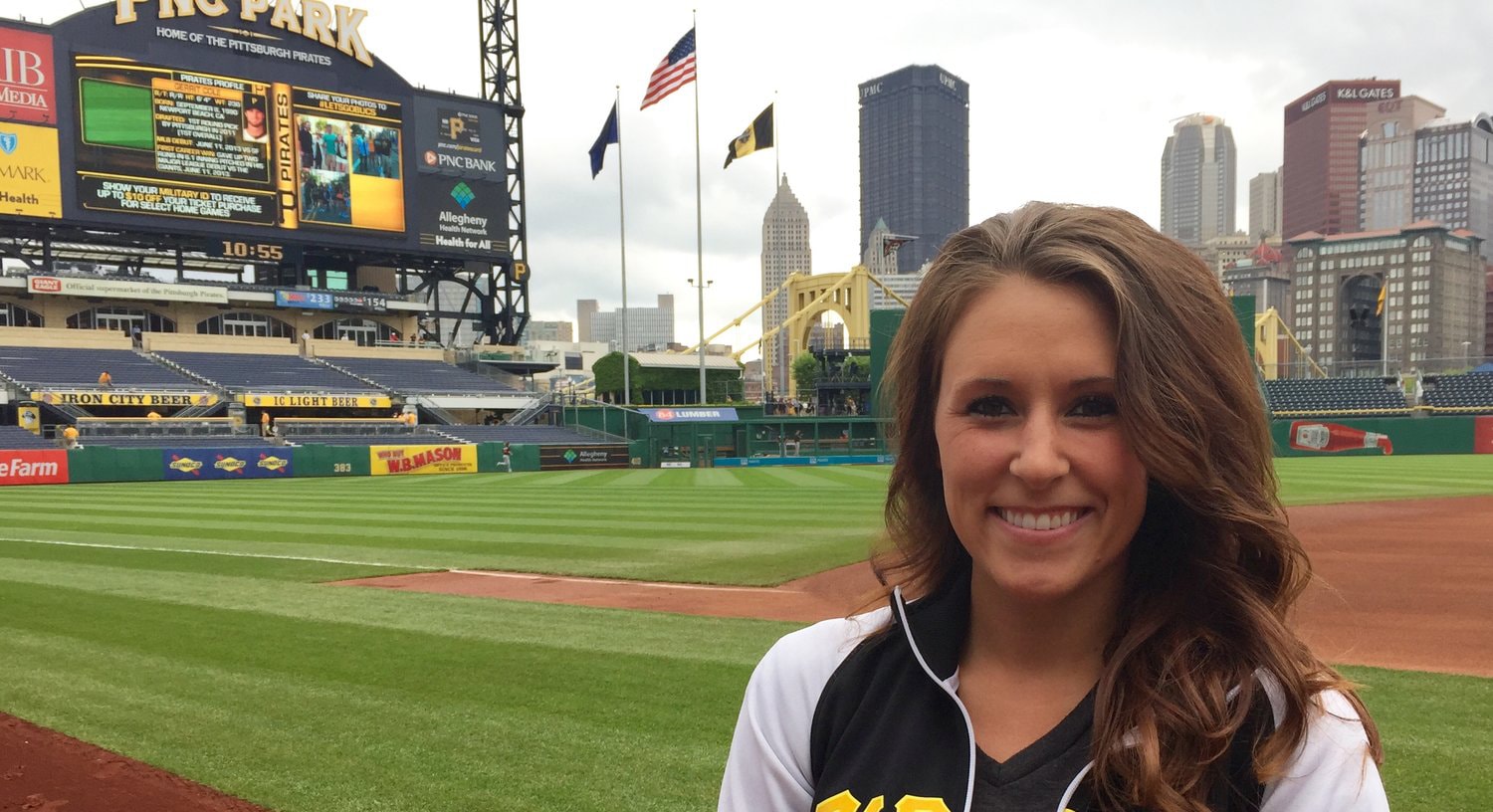 Photo of a woman standing on the field at PNC Park in Pittsburgh wearing a Pittsburgh Pirates zip up jacket. 