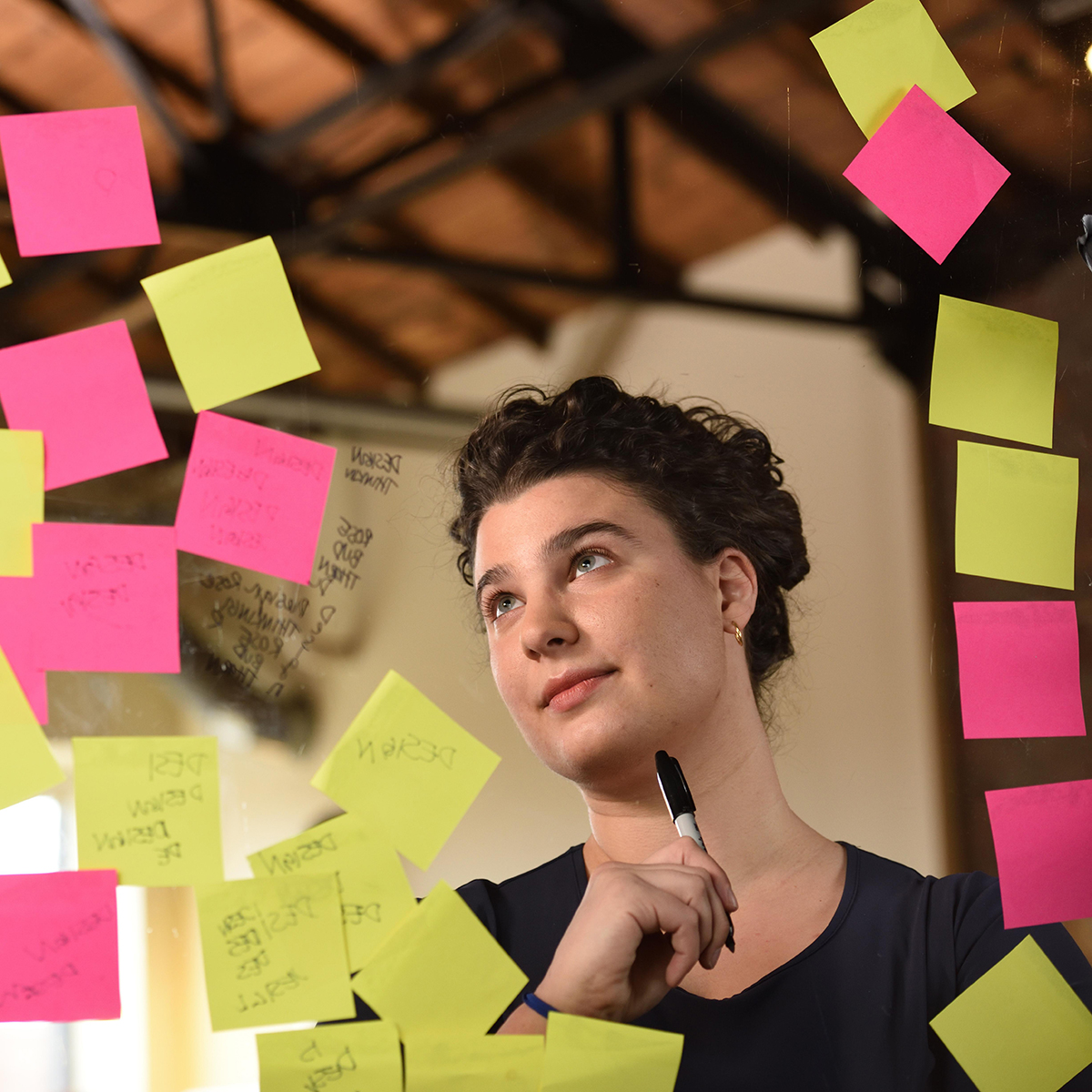 Photo of a young white brunette woman writing on clear glass covered in Post-It notes