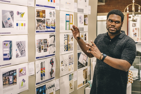 Photo of a male Chatham University student standing in front of a posterboard presenting a project with diagrams.  