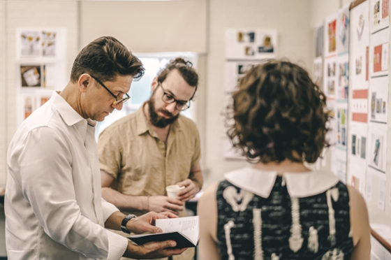 Photo of three people standing together looking at a shared journal and poster board.