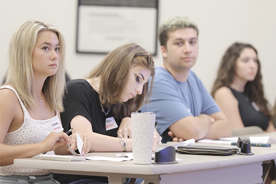 Several students seated together in a classroom, paying attention to an off-screen presentation