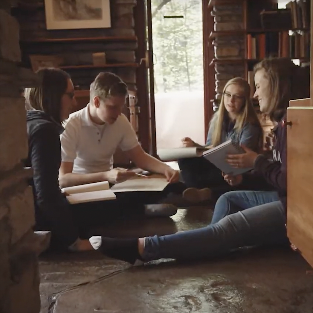 Photo of a group of students seated on the floor in Fallingwater, sketching and talking together