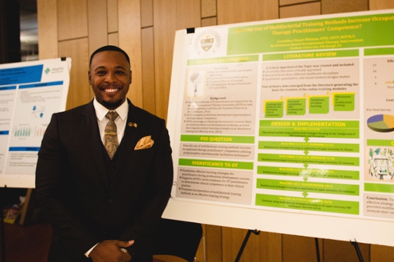 Photo of a smiling man in black suit and tie, posing in front of poster presentation. 