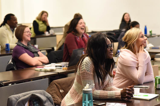 Photo of a group of Chatham University students seated in a lecture hall, smiling and interacting with an instructor out of frame.