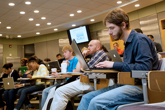 Photo of a Chatham University student sitting in a Chatham Eastside lecture hall taking notes on his laptop.