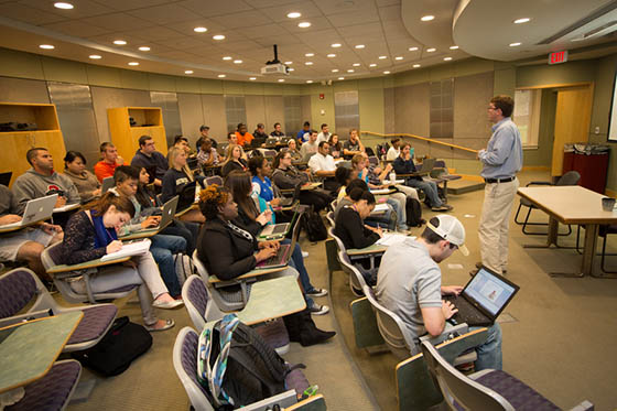 Photo of students in a lecture hall, with a professor at the front of the class