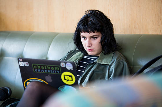 Photo of a Chatham University student sitting on a couch in Cafe Rachel, working on her laptop