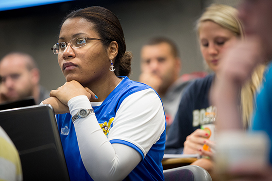 Photo of a Chatham University student sitting in a lecture hall listening to a professor with a laptop in front of her. 