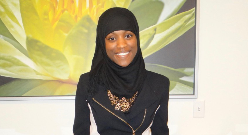 Photo of a Chatham University student wearing a hijab, smiling in front of artwork. 
