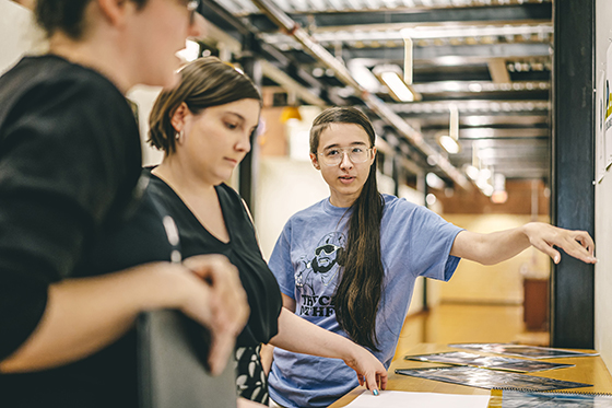 Photo of three people standing in a design lab consulting printed designs. 