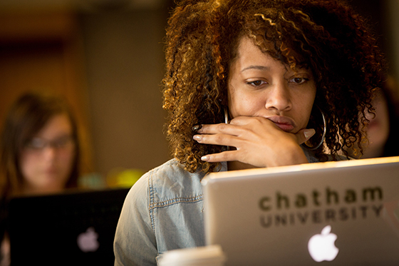 Photo of a woman working on her laptop with a Chatham University sticker in a lecture hall