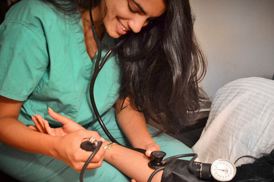 Photo of a nurse in green scrubs taking a patient's blood pressure with a stethoscope. 