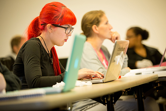 Photo of a student with glasses and bright red hair, typing on her laptop during class