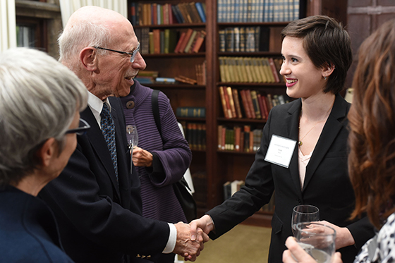 Photo of a female Chatham University student with a name tag and blazer, shaking the hand of a man in a suit at a networking event. 