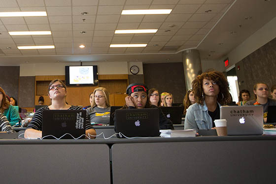 Photo of Chatham University students sitting in a lecture hall taking notes on laptops in tiered seating.