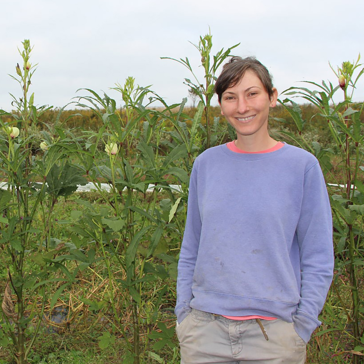 Photo of a woman standing in front of crops at Eden Hall Farm smiling.