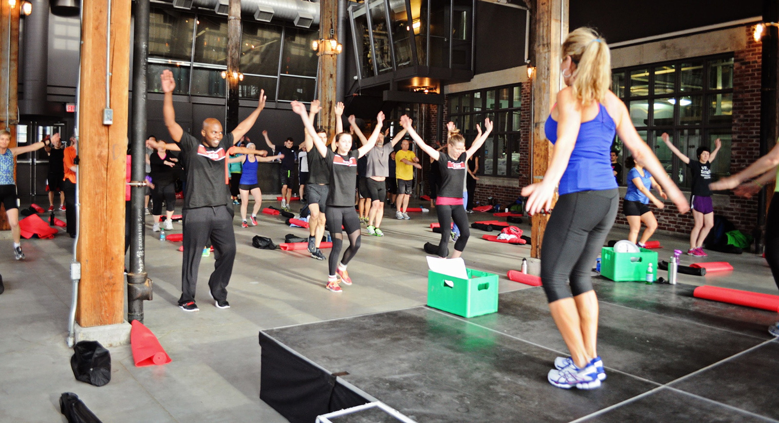 Photo of a fitness instructor leading a group of people in jumping in industrial space. 