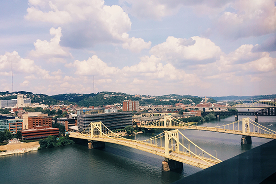 Photo of the skyline of Pittsburgh, with a river and yellow bridges