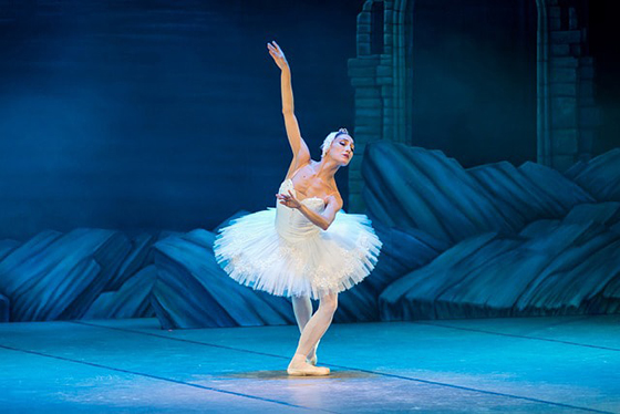 Photo of a ballerina dancing in Swan Lake, wearing a white costume and head piece. 