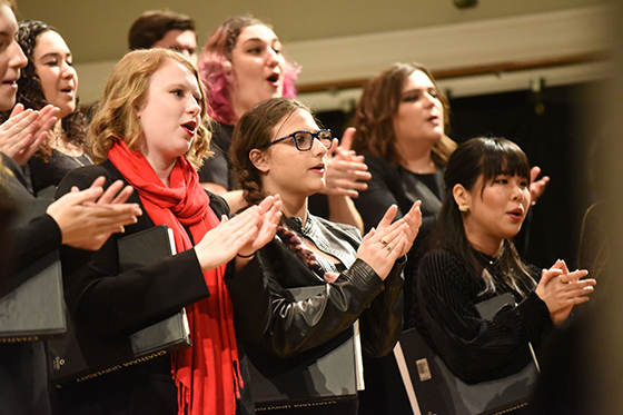 Photo of Chatham University music students standing on risers in a choir with music and matching black outfits. 