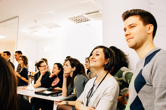 Photo of a group of professionals standing and sitting in a conference room, looking toward an off-frame speaker.