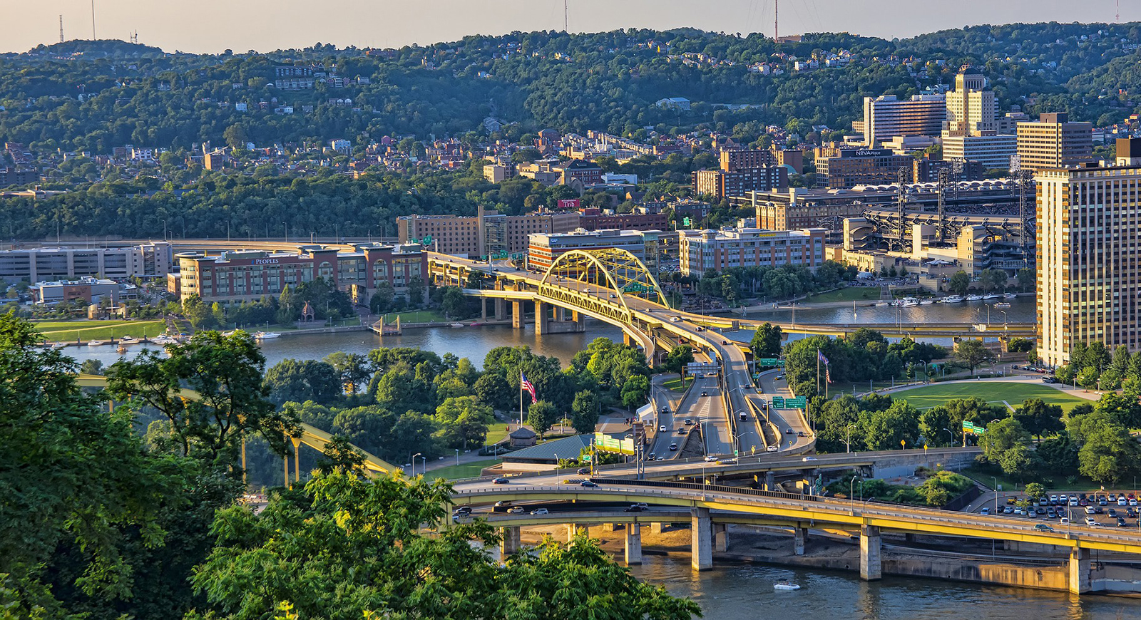 Photo of Pittsburgh's yellow bridges and rolling hills framing rivers at sunset. 