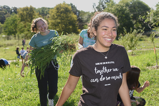 Photo of smiling Chatham University students working at Eden Hall Farm in the field removing weeds.