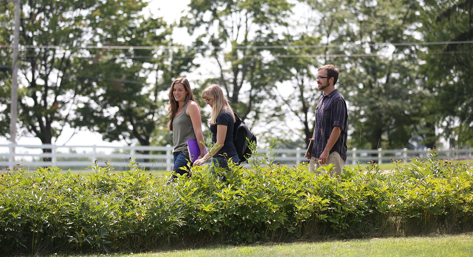 Photo of Chatham University students walking to class on the Eden Hall Campus through green fields holding books and binders. 