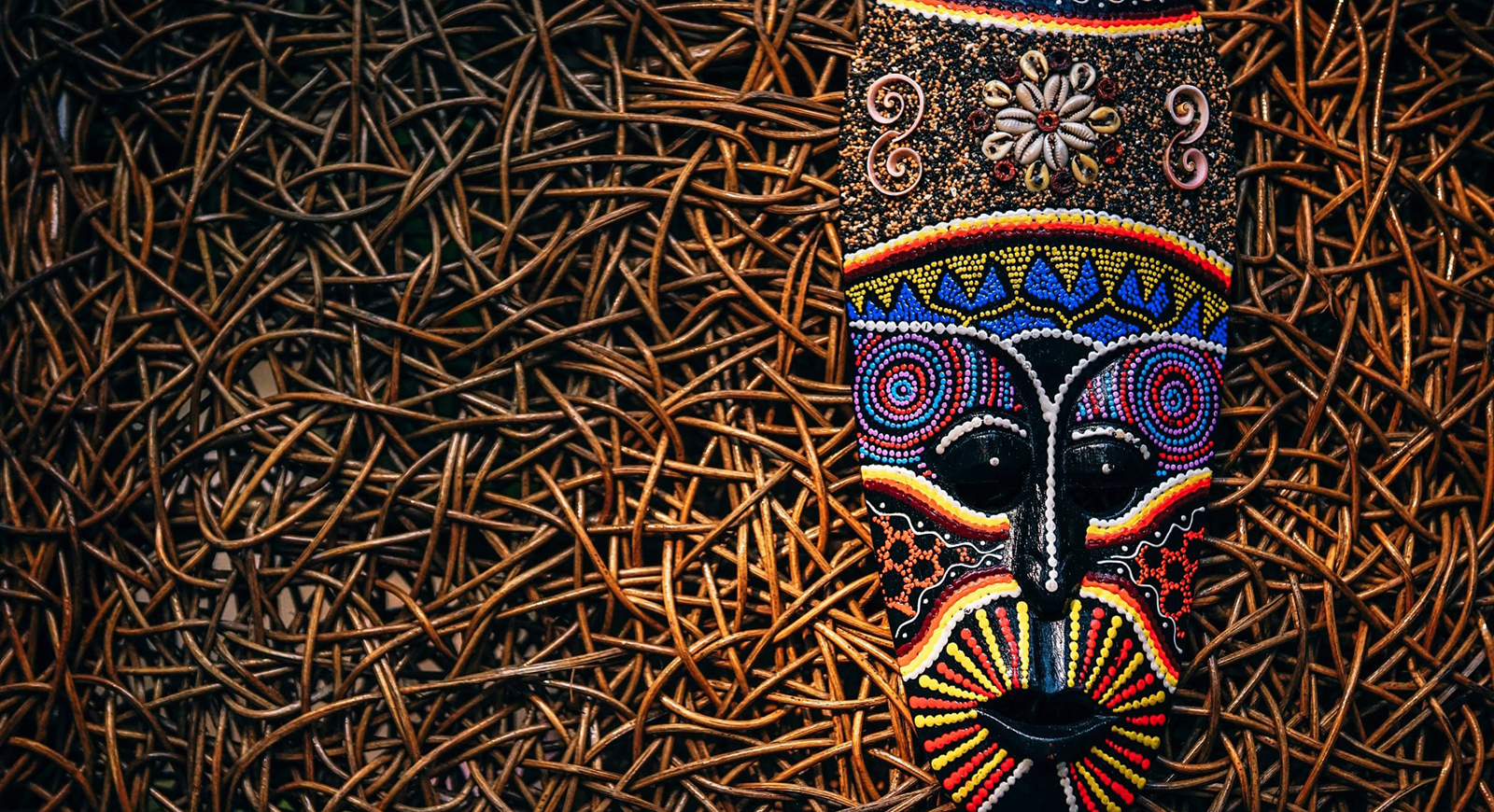 Photo of a colorful tribal mask resting on a bed of twigs. 