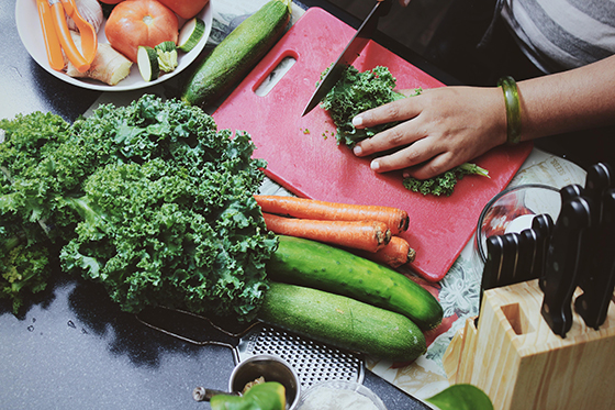 Photo from above showing a person chopping kale on a red cutting board surrounded by other vegetables