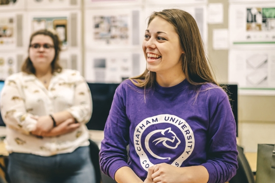 Photo of a smiling female student wearing a purple Chatham University shirt in a classroom.