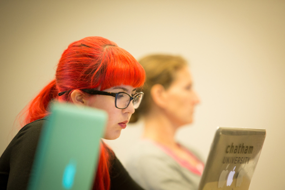 Photo of a female Chatham University student writing on her laptop during a lecture.