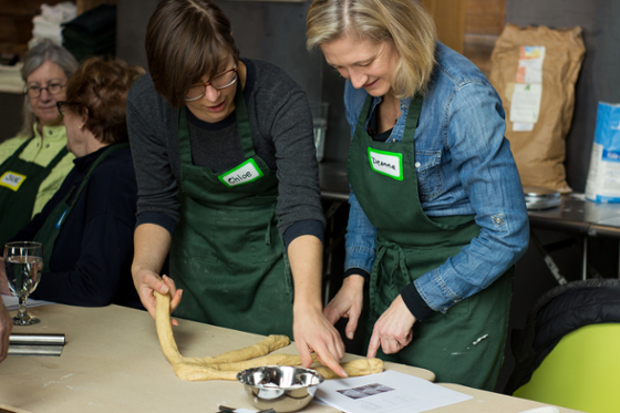 Photo of a woman helping another woman make challah bread at Eden Hall Campus