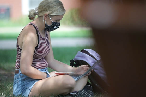 Photo of a woman working on a laptop, wearing a mask, and sitting outside on Chatham University's Shadyside Campus