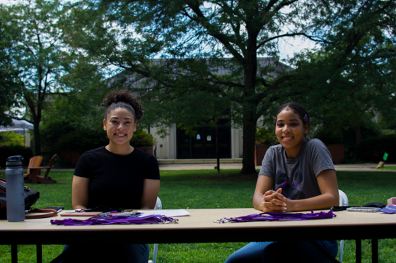 Photo of two Chatham University female students smiling for the camera behind a table, at an activities fair