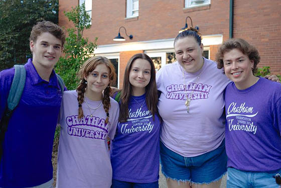 Group of five students in purple pose together and smile for a photo