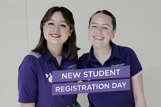 Two student volunteers wearing purple smile together for a photo. 'New Student Registration Day' is written on a purple banner in front of them.