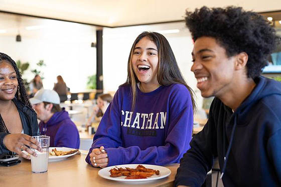 A group of three students smile and laugh at a dining hall table
