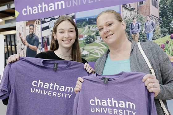 A student and parent stand together, holding Chatham University purple t-shirts and smiling