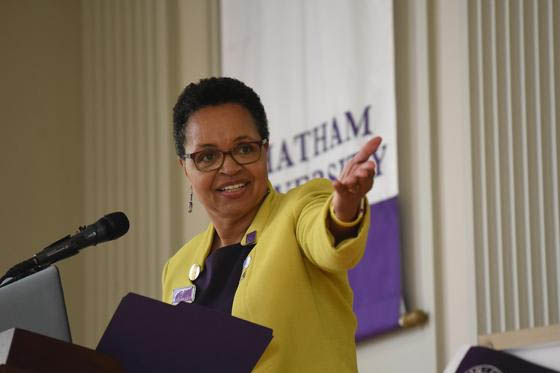 Photo of a woman speaking at a podium, gesturing to something off camera