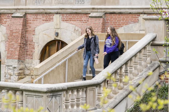 Photo of two female Chatham University students walking down a grand staircase outdoors on Shadyside Campus